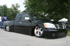 a black truck parked on the side of a road next to some trees and people