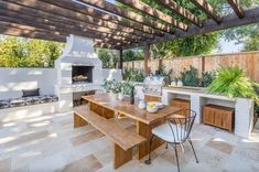 an outdoor kitchen and dining area with wood table, grilling oven and seating bench