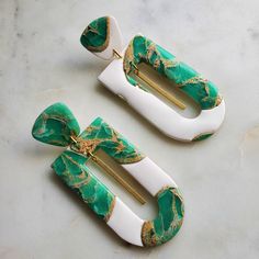 two green and white hair clips on a marble counter top with gold detailing, one has a large bow at the end