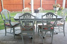 a dining table with chairs around it in front of a fenced yard and flowers