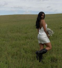 a woman standing in the middle of a field holding a bouquet of flowers and wearing black boots