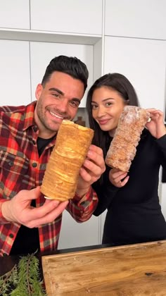 a man and woman posing for a photo while holding up a large piece of bread