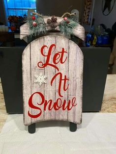 a wooden sign that says let it snow with pine cones on top and red lettering