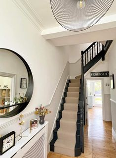 there is a mirror on the wall next to some stairs in this house with white walls and wood flooring