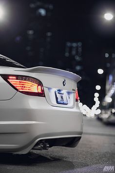 the back end of a white car parked in a parking lot at night