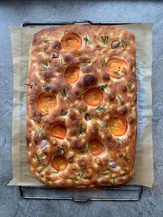 a square shaped pizza with tomatoes and olives on it sitting on a piece of parchment paper