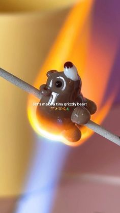 a small toy bear sitting on top of a matchstick in front of a colorful background