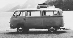 an old van parked on the side of a body of water with mountains in the background