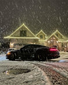 a black car parked in front of a house on a snowy night with christmas lights