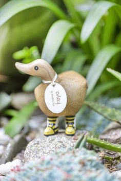 a small wooden duck sitting on top of a rock next to some plants and rocks