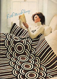 a woman sitting on a couch reading a book while holding a blanket over her head