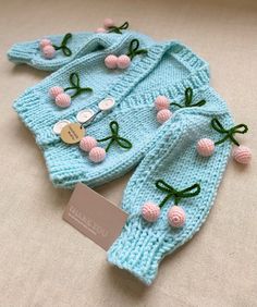 two knitted sweaters with pink flowers and green leaves on the top, one has a tag attached to it