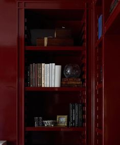 a red bookcase with many books on it in a room that is painted dark red