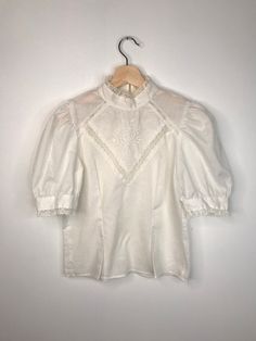 "Beautiful vintage blouse with mock neck, puffed sleeves, embroidery and lace  Very good condition  50% cotton, 50% polyester  Fits XS -S  Shoulders 13\" Chest 17.5\"  Length 20.5 \"" Fitted Bishop Sleeve Blouse With Floral Embroidery, Fitted Cotton Tops With Bishop Sleeves, Fitted Cotton Top With Bishop Sleeves, Fitted Blouse With Floral Embroidery And Bishop Sleeves, Fitted Cotton Blouse With Lace Sleeves, Cotton Embroidered Puff Sleeve Blouse, Vintage White Top With Lantern Sleeves, Vintage White Lantern Sleeve Top, White Vintage Lantern Sleeve Top