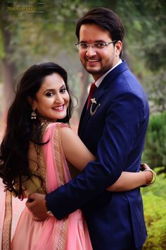 a man in a blue suit and tie hugging a woman wearing a pink lehenga