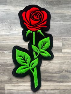 two red roses with green leaves sitting on top of a wooden floor