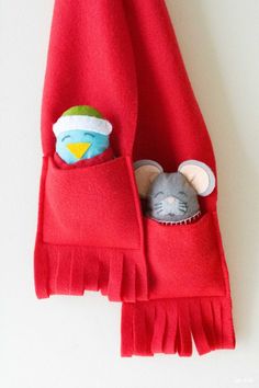 a stuffed mouse in a red pocket on a white wall with fringes and a green ball