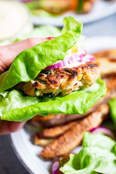 a person is holding up a chicken burger with lettuce and red onion on it