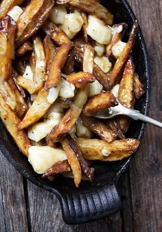 french fries in a cast iron skillet on top of a wooden table with a spoon