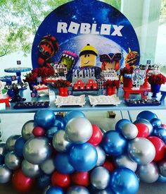 a table topped with balloons and decorations next to a sign that says roblox