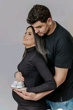 a man and woman standing next to each other with their arms around the pregnant belly