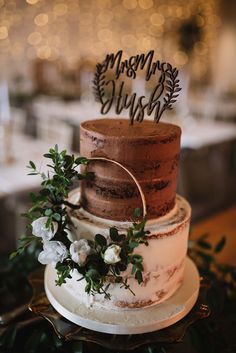 a three tiered wedding cake with greenery on top and mr and mrs sign