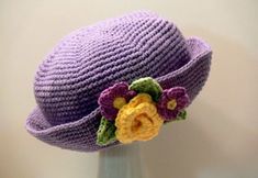 a purple crocheted hat with flowers on it's brimmed crown