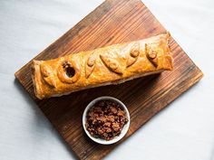 a wooden cutting board topped with a loaf of bread next to a bowl of raisins