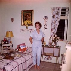 a woman standing next to a bed in a room with pictures on the wall behind her