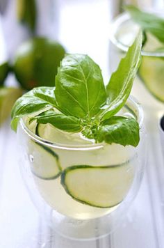 a glass filled with water and green leaves on top of a white table next to limes