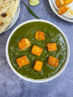 a white bowl filled with green curry and tofu cubes on top of it