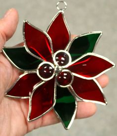 a hand holding a christmas ornament with red and green flowers on it's side