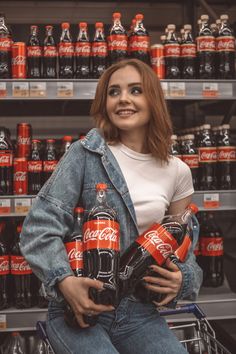 a woman sitting on a shopping cart holding two coca - cola bottles in her hands