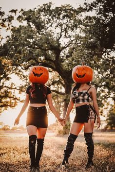 two girls in costumes holding hands with pumpkins on their heads, both wearing high heeled boots