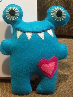 a blue stuffed animal with big eyes and a heart on it's chest next to a card