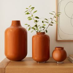 three vases with plants in them sitting on a table next to a framed painting