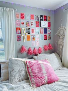 a white bed with pink pillows and pictures on the wall above it, in front of a window