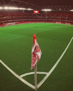 an empty soccer field at night with the lights on and one flag in the corner