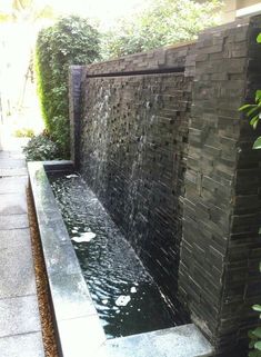 an outdoor fountain with water flowing from it's sides and surrounded by greenery