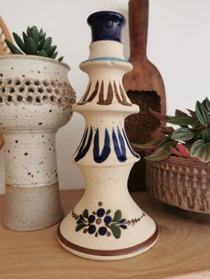 three ceramic vases sitting on top of a wooden table next to plants and baskets