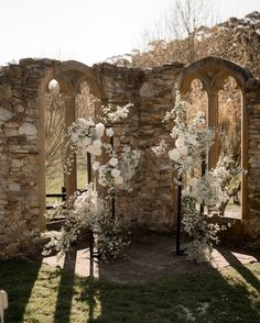 an outdoor ceremony setup with white flowers and greenery on the aisle, surrounded by stone arches