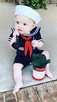 a baby sitting on the ground next to a potted plant wearing a sailor outfit