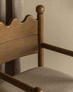 a close up of a wooden chair with a beige fabric seat pad and armrests