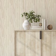 a white vase with green leaves on top of a wooden cabinet next to a wall