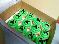 a box filled with green cupcakes covered in frosting and black icing