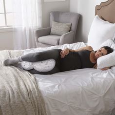 a woman laying on top of a bed next to a white chair and window in a bedroom