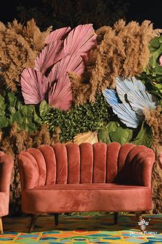 a red velvet couch sitting in front of a wall with flowers and plants on it