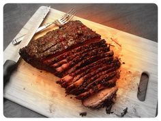 a piece of meat sitting on top of a cutting board next to a knife and fork