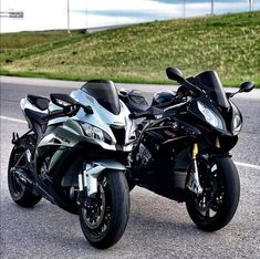 two motorcycles are parked on the side of the road in front of a grassy hill