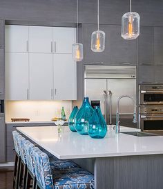 a kitchen island with stools and lights hanging from it's ceiling above it